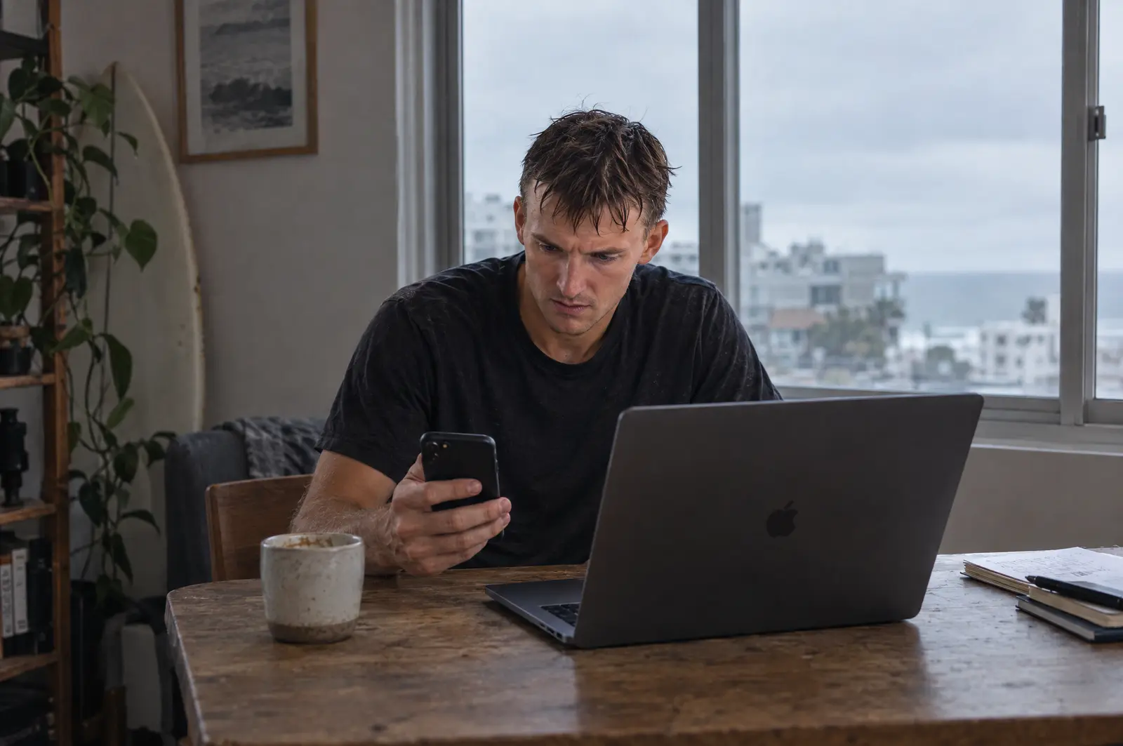 Sem a Sapiens: o mesmo homem, num sábado cedo, em frente ao notebook e com o celular na mão, sério.