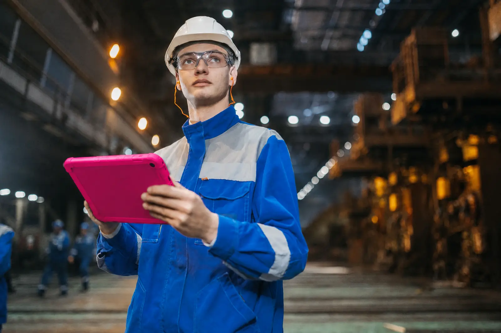 Indústrias de médio porte: um operário de capacete confere um tablet fúcsia na fábrica.